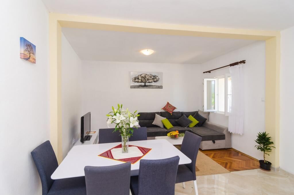 Un comedor con una mesa y sillas blancas, un sofá con cojines, un cuadro en la pared y una planta pequeña.