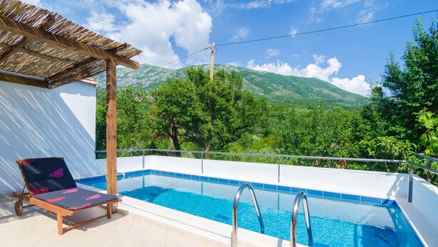 A swimming pool with a chair and a pergola, surrounded by lush greenery and mountains. - Villa Dalmatian Gem (Konavle)