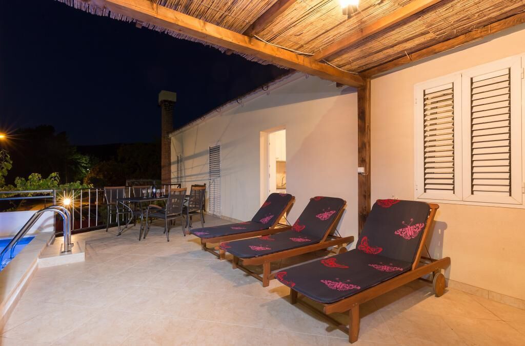 Un espacio al aire libre techado con piscina, sillones de descanso y una mesa con sillas.