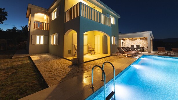 Una casa de dos plantas con piscina, mobiliario de exterior y un patio de piedra.