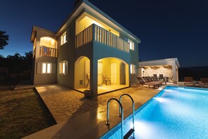 Una casa de dos plantas con piscina, mobiliario de exterior y un patio de piedra.