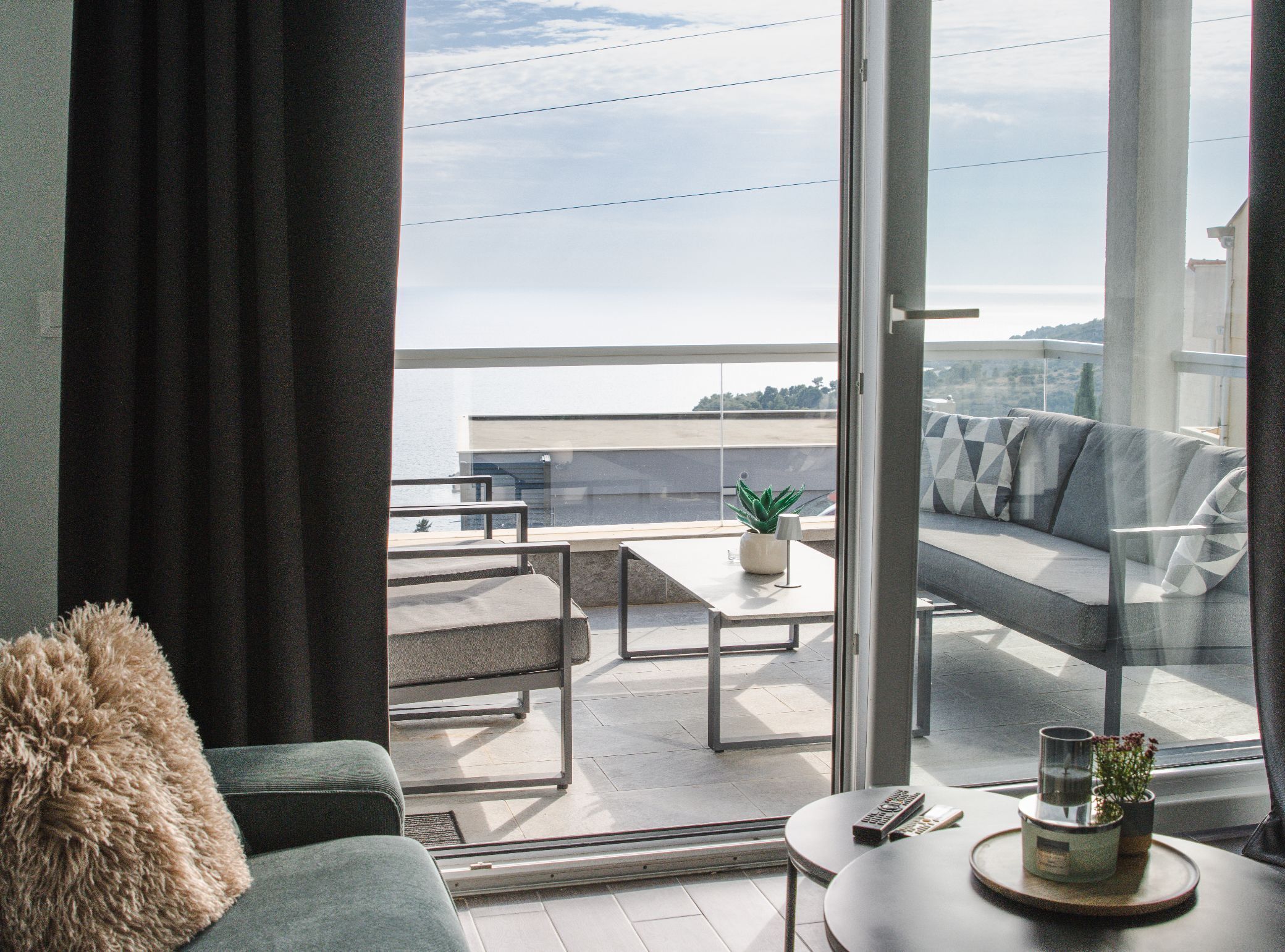 A modern living room with a sofa, a coffee table, and a balcony with a view of the sea.