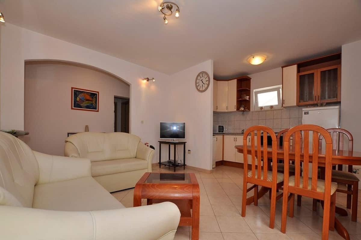A living room with a sofa, a television, and a dining area with wooden chairs and a table.