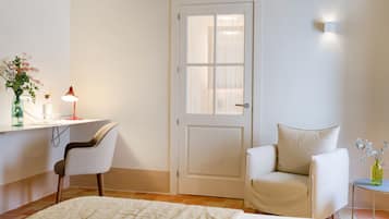 Habitación de hotel con cama, escritorio con silla, una mesita de noche con lámpara y una puerta.