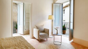 A bedroom with a bed, a chair, a small table, and a window with a view of the outside.