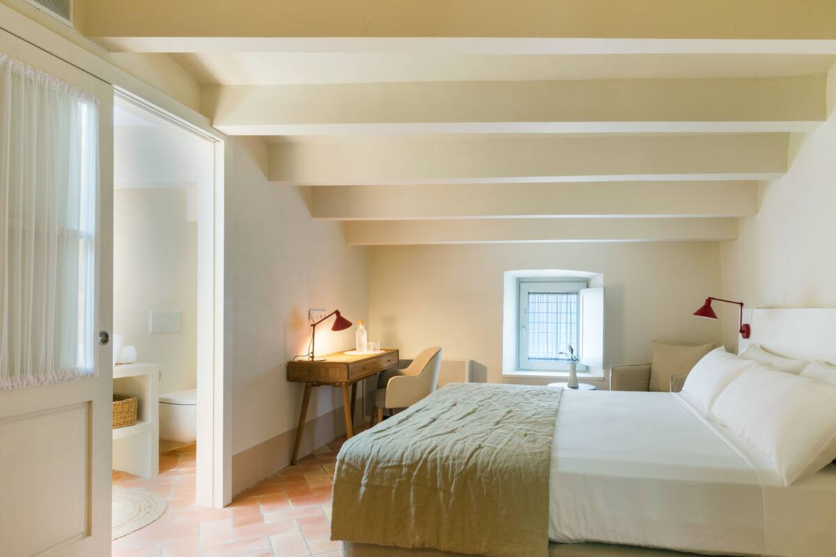 A bedroom with a bed, desk, chair, and a window.