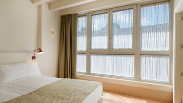 A hotel room with a large bed, a window with curtains, and a wall-mounted light.