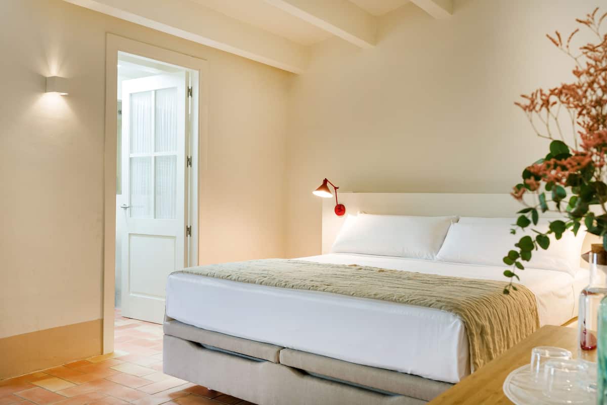 A bedroom with a bed, bedside table, lamp, and a door leading to another room.