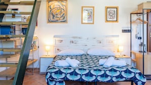 A hotel room with a bed, two bedside tables, a nightstand, a wardrobe, a staircase, and artwork on the walls.