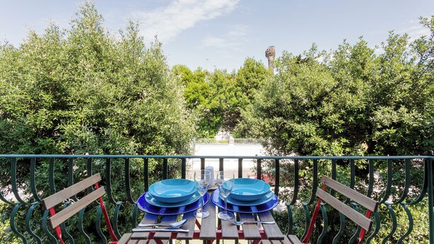 An outdoor dining area with a table set for two, surrounded by greenery and a railing.