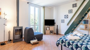 A cozy room with a wood-burning stove, a comfortable sofa, a bed with a patterned bedspread, a flat-screen TV, and a staircase.