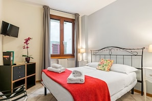 Habitación de hotel ordenada con cama, televisor, escritorio y ventana con cortinas.