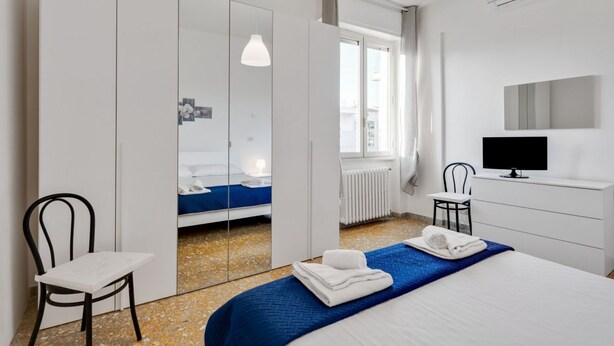 A modern hotel room with a bed, a desk, a chair, a TV, and a wardrobe. - Lulli Cozy Apartment with Balcony (Florence)