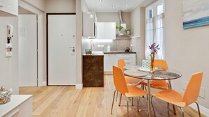 A modern kitchen with white cabinets, a central island, and orange chairs around a glass table.
