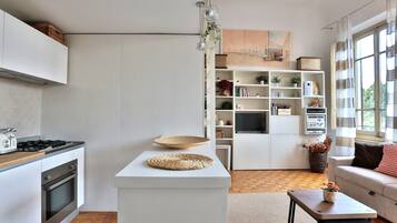 Una cucina moderna con mobili bianchi, piano cottura integrato e zona pranzo con tavolo rotondo e sottopiatti in fibra naturale.