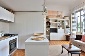 Una cocina moderna con muebles blancos, estufa integrada y zona de comedor con una mesa redonda y un mantel tejido.