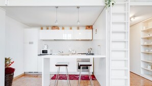 A modern kitchen with white cabinets, a central island with stools, a microwave, and a kettle. - Piazza San Marco Studio Flat (Florence)