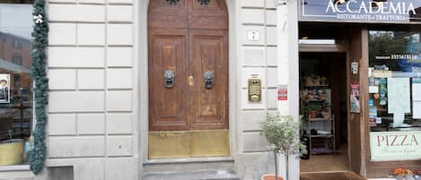 Un bâtiment doté d’une grande porte à double battant en bois, d’une petite plante en pot et d’une devanture avec une enseigne indiquant « pizzeria ».
