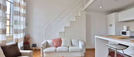 A modern living room with a sofa, coffee table, and a staircase leading to a kitchen area.