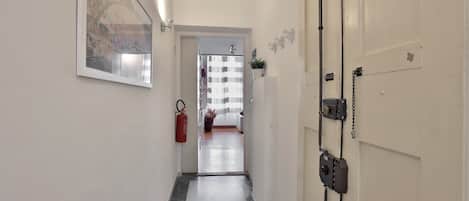 A hallway with a fire extinguisher, a door with a chain lock, and a view into a room with a shower.
