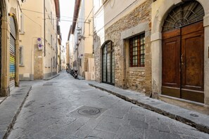 A narrow cobblestone street flanked by historic stone buildings with arched windows and wooden doors.