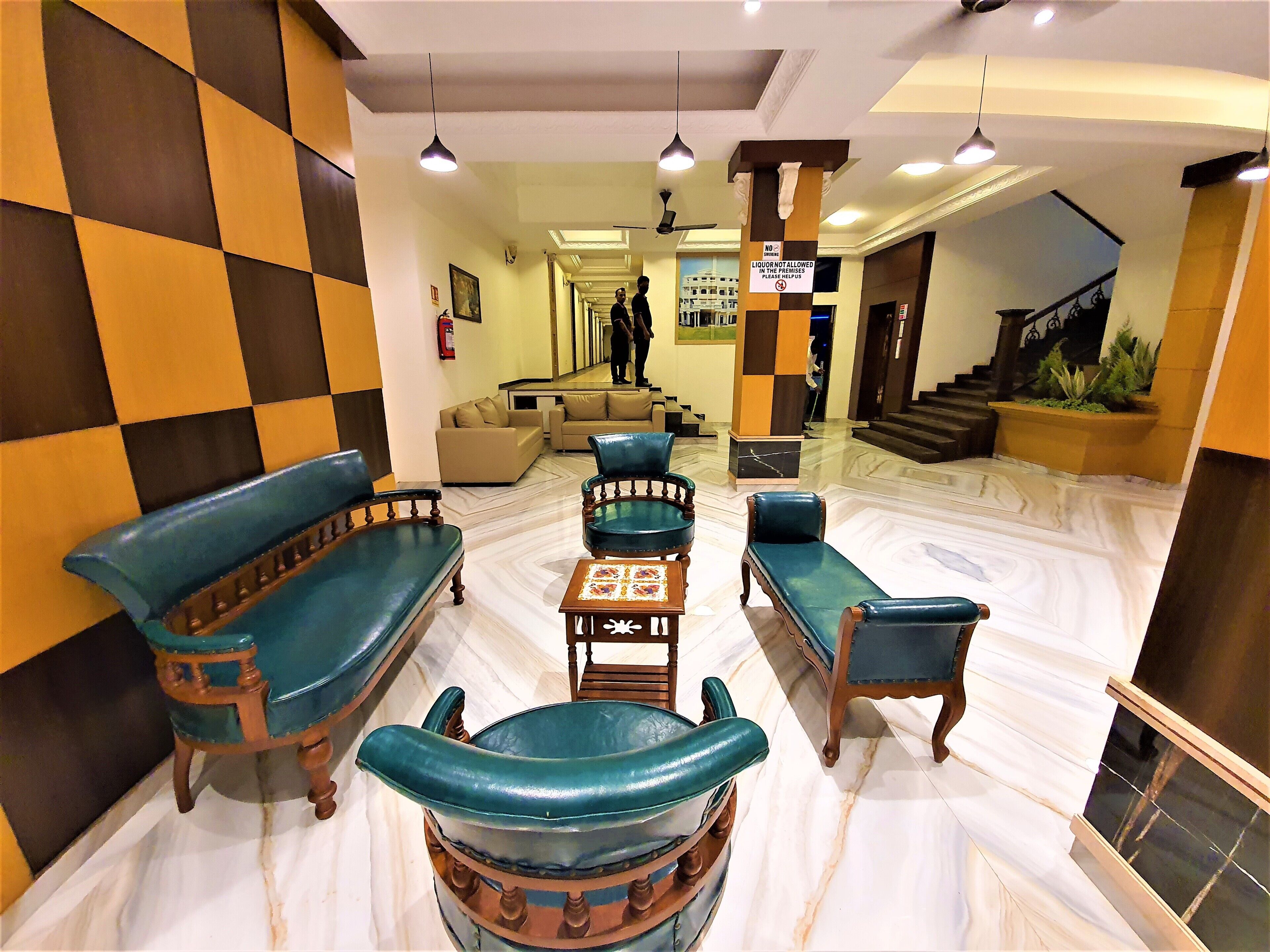 A lobby with a checkered wall, a sofa, chairs, a small table, and a staircase.