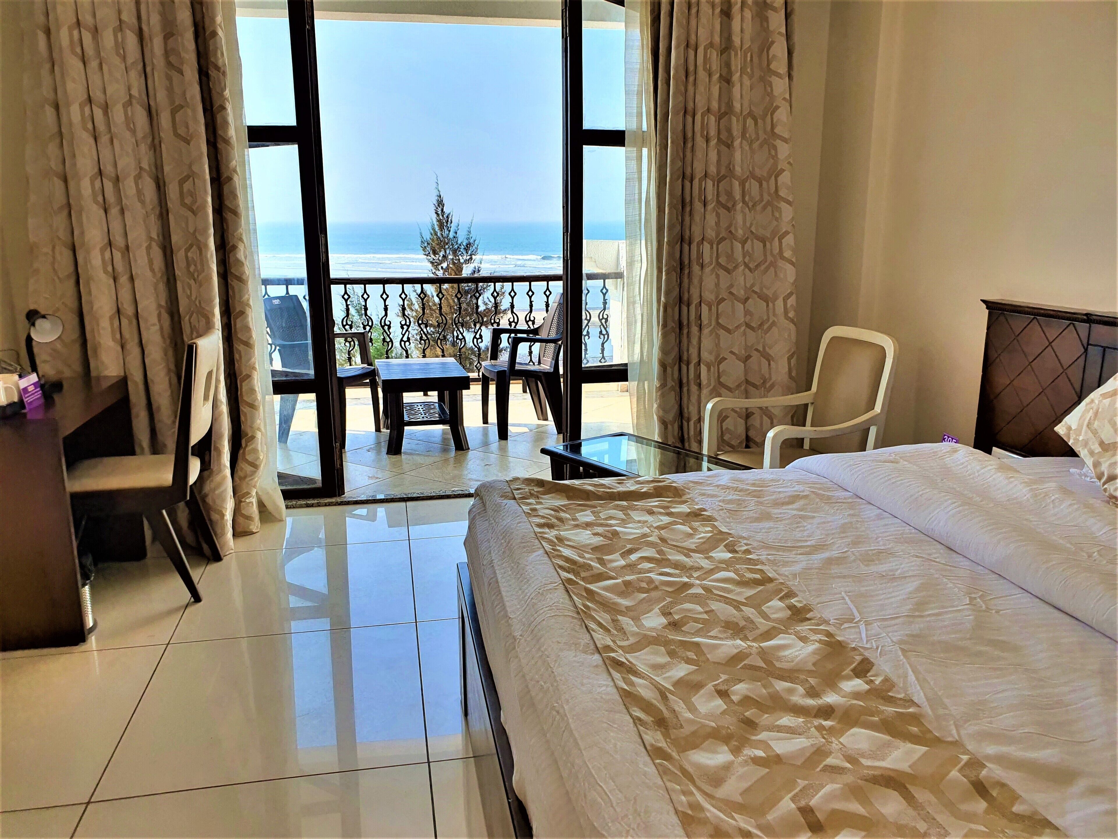 A hotel room with a bed, a desk, and a balcony with a view of the ocean.