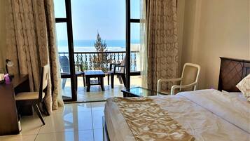 Habitación de hotel con cama, escritorio y balcón con vista al océano.