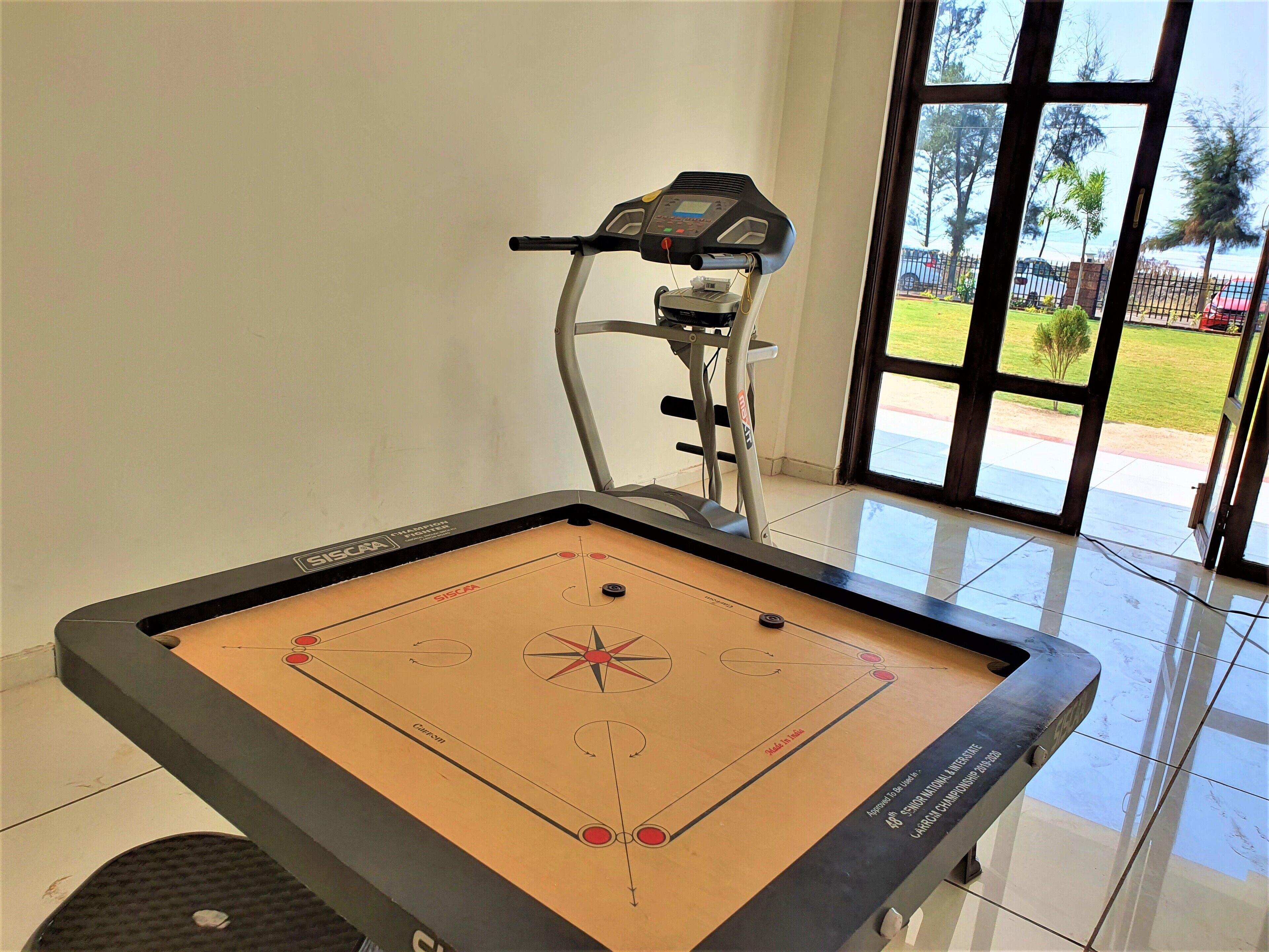A room with a shuffleboard table, a treadmill, and a large window with a view of a green landscape.