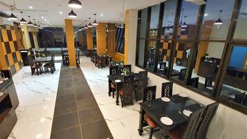 Un restaurant doté d’une allée centrale, de tables, de chaises, de luminaires suspendus et de grandes fenêtres.