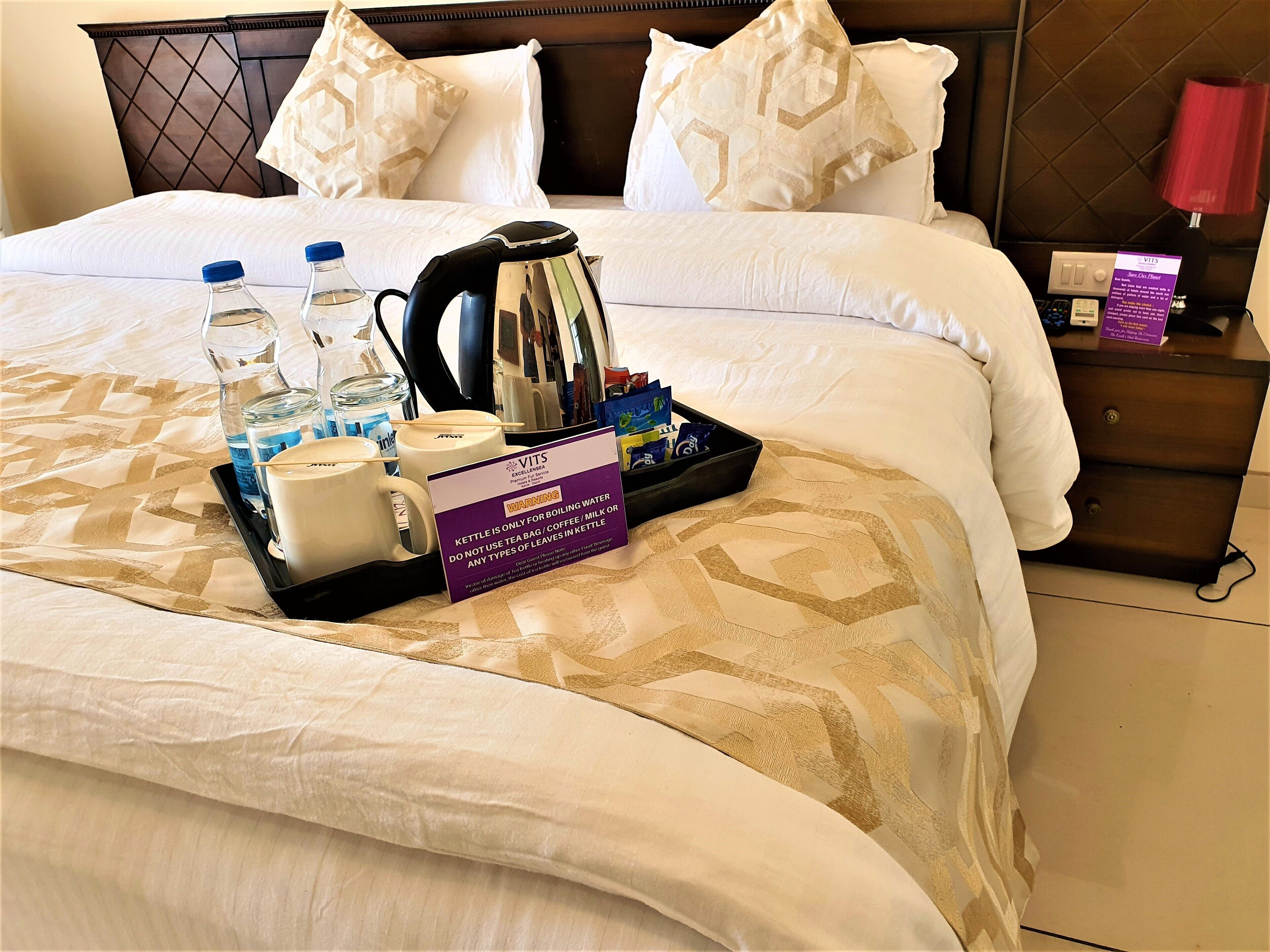 A neatly made bed with a tray of breakfast items including tea bags, a kettle, and bottled water.