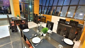 A modern dining area with glass partitions, wooden furniture, and a view of the city at night. - VITS Excellensea Karde Beach (Dapoli)