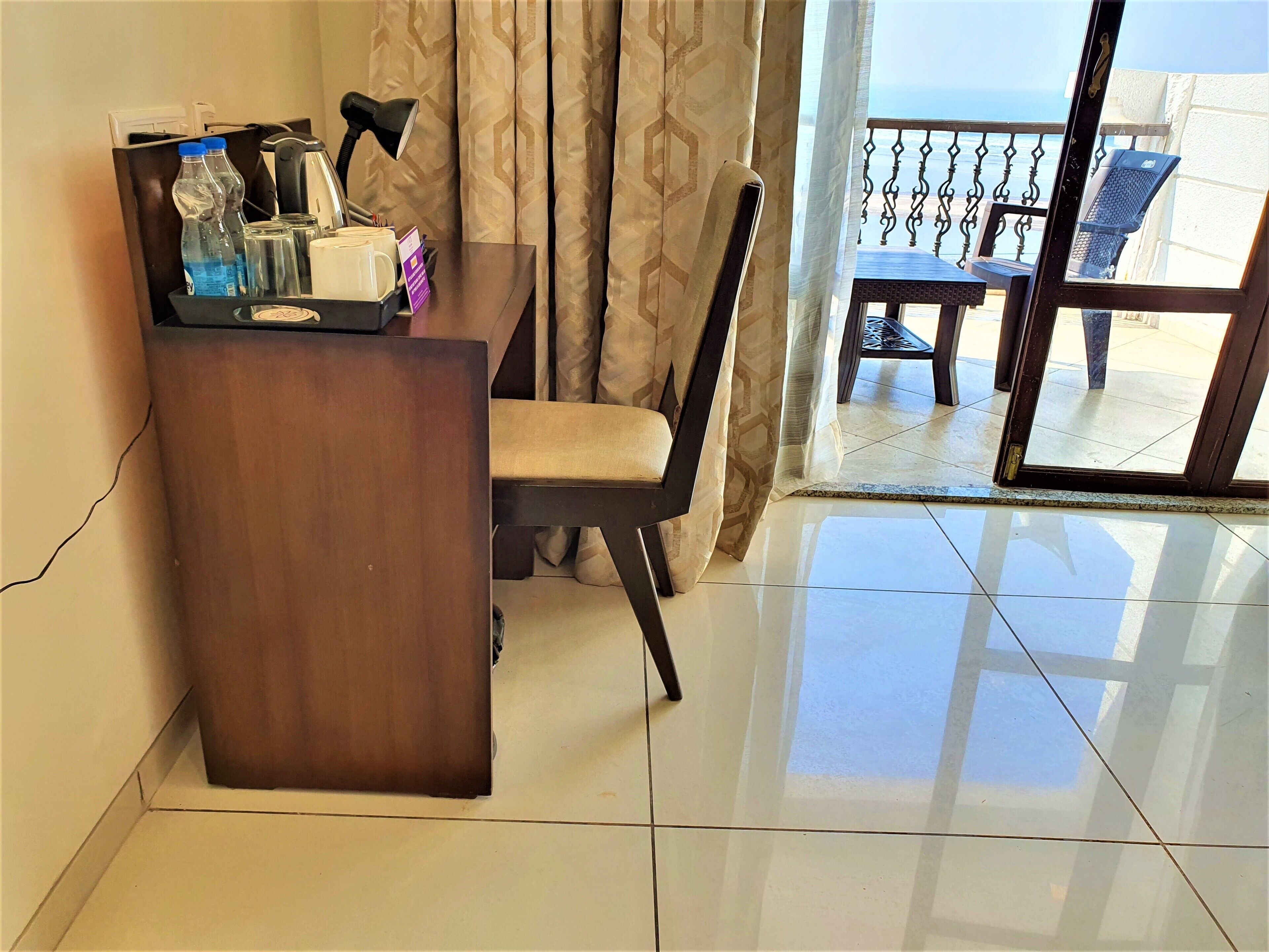 Habitación de hotel con escritorio de madera, una silla, una mesa y vistas al balcón.