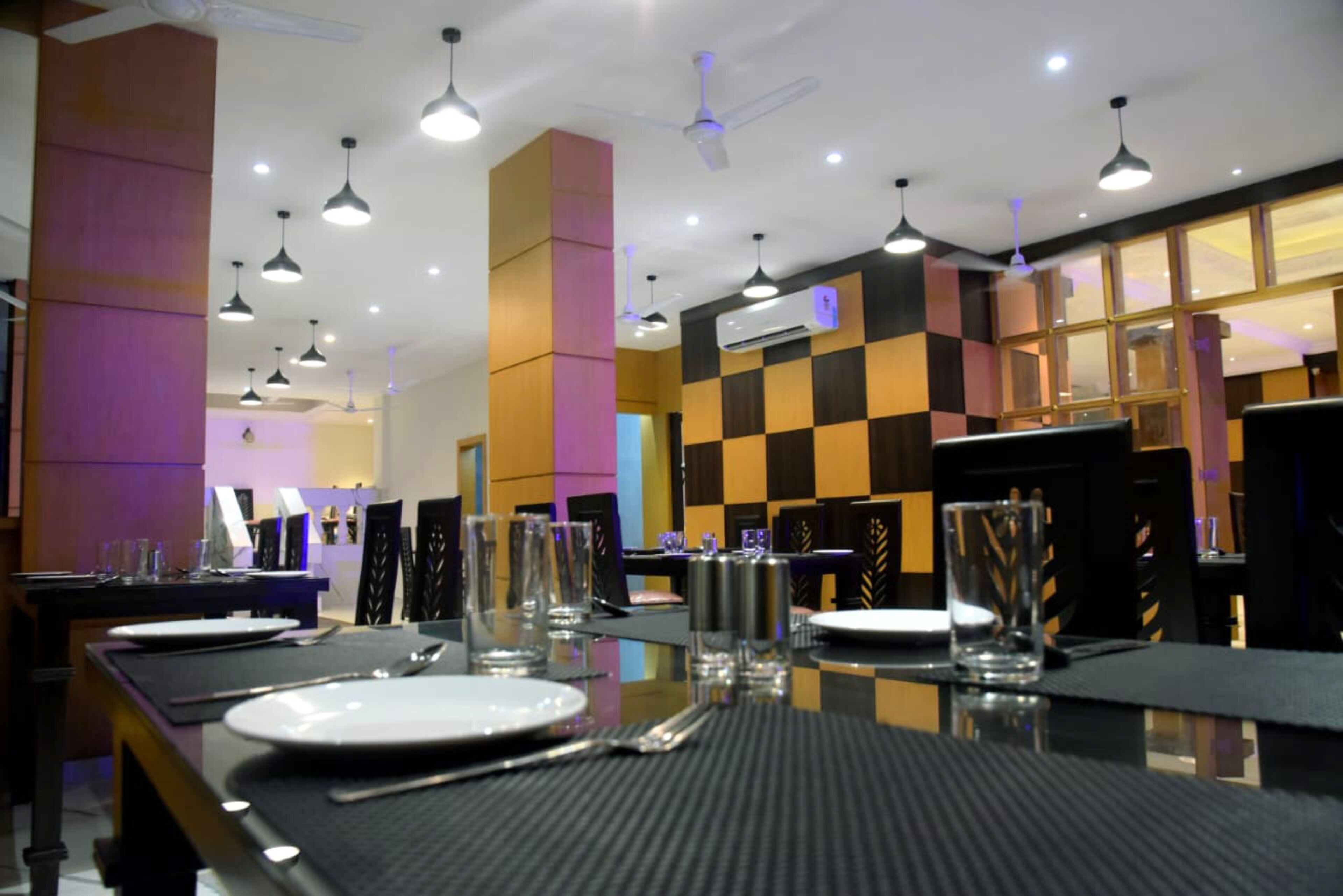 A restaurant with tables set for dining, ceiling fans, and a checkered wall pattern.