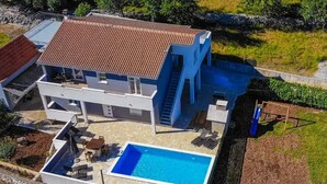 Una casa de dos pisos con piscina, mobiliario exterior y una escalera que lleva al piso superior.