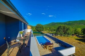 A balcony with a pool, outdoor furniture, and a view of green hills. - Holiday Home Zen in Primorski Dolac (Primorski dolac)