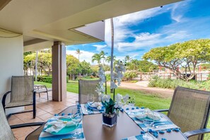 Un comedor con una mesa lista para dos, sillas y vistas a un jardín con palmeras y una piscina.