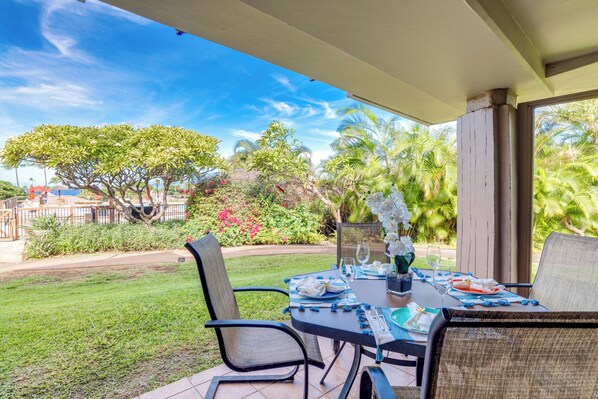 Un patio al aire libre con una mesa lista para comer, rodeado de sillas y una zona techada.