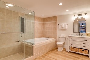 Un baño moderno con ducha de vidrio, bañera independiente, inodoro y tocador con cajones y cestas.