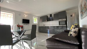 Eine moderne Küche mit Einbauofen und Mikrowelle, ein Essbereich mit Glastisch und Stühlen sowie ein Wohnzimmer mit Sofa und Fernseher.