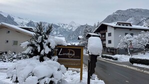 A sign for Landhaus Daum hotel with a view of snow-covered mountains. - Description (Schwendau)