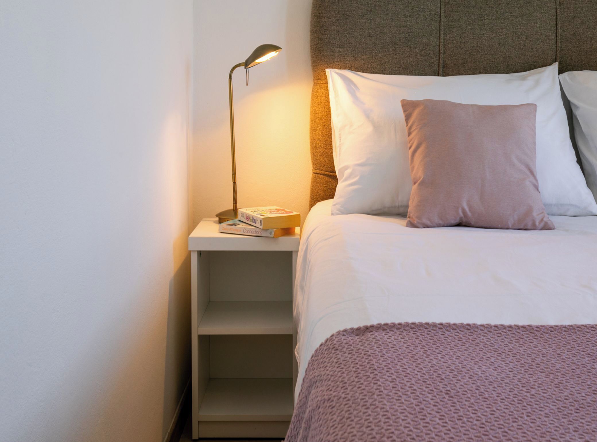 A neatly made bed with pillows, a bedside lamp, and a small shelf with books.