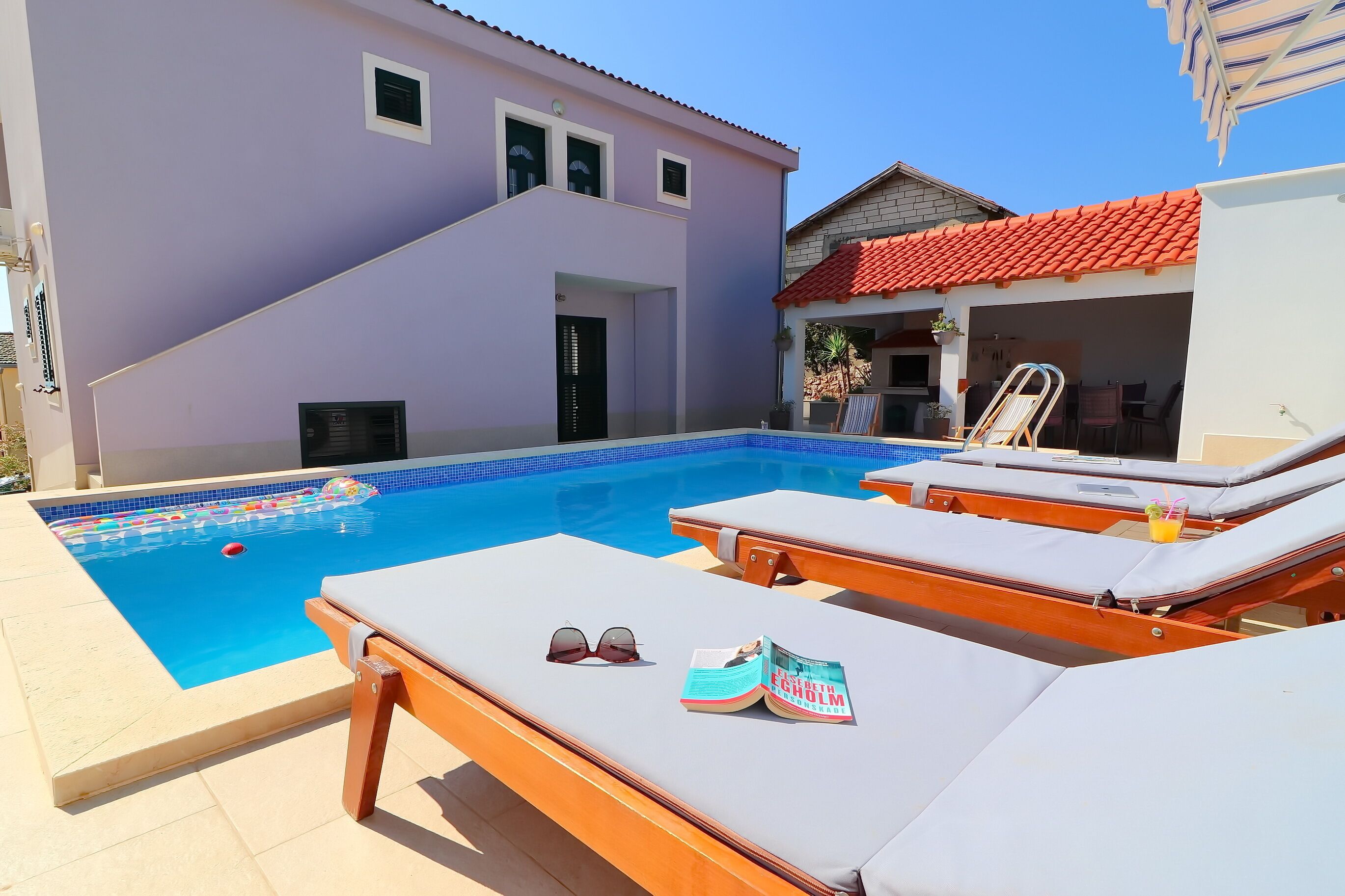 A swimming pool with lounge chairs, a magazine, and sunglasses on one of the chairs.