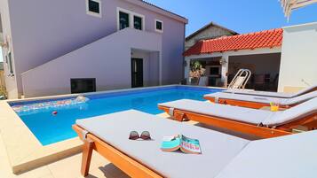 A swimming pool with lounge chairs, a magazine, and sunglasses on one of the chairs.