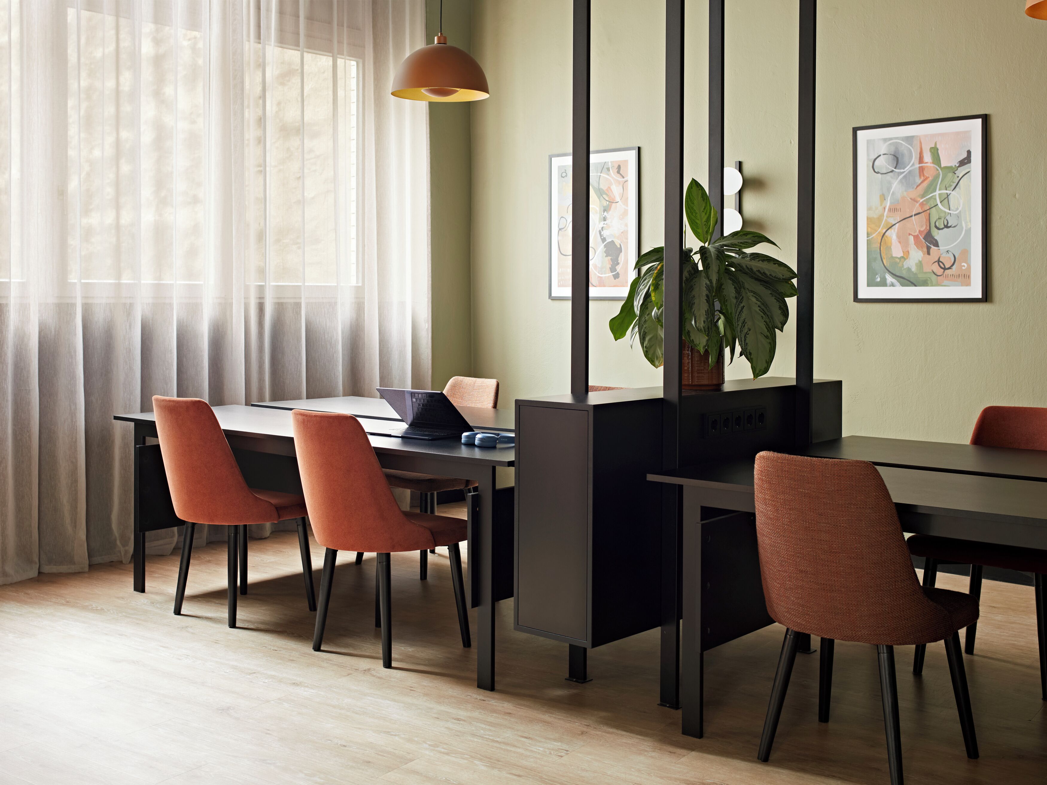 A modern conference room with a long table, black chairs, a laptop, a potted plant, and abstract art on the walls.