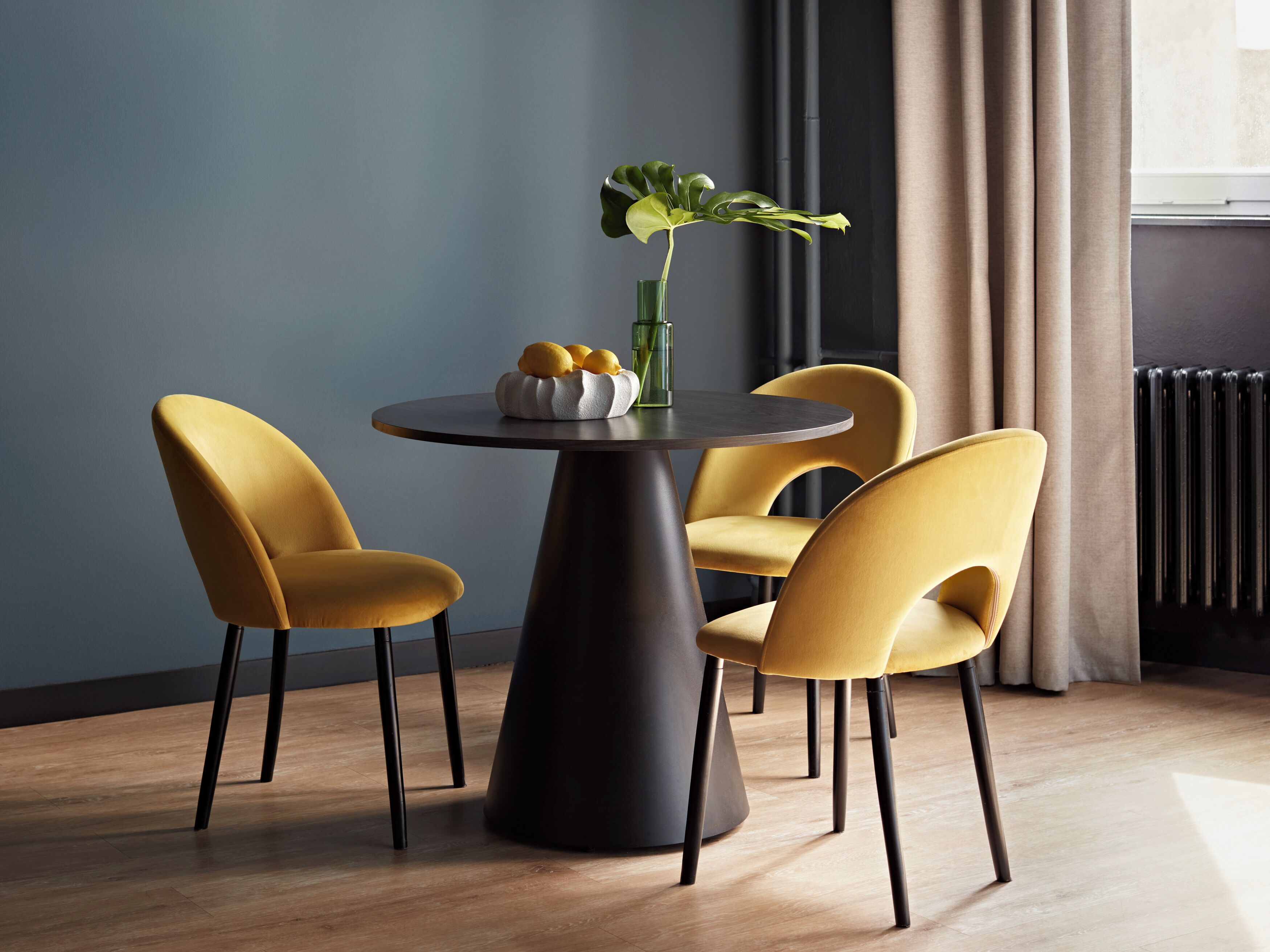 Un comedor moderno con una mesa redonda, dos sillas amarillas y un jarrón con una planta.