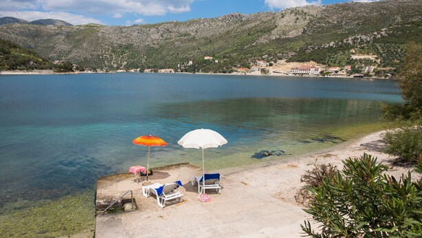 A beach with clear water, a few umbrellas, and lounge chairs.