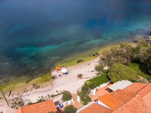 Vista aérea de una propiedad costera con playa, aguas cristalinas y un pequeño patio con sombrillas y sillas de descanso.
