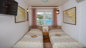 A bedroom with two single beds, a television, a map on the wall, and a window with curtains.
