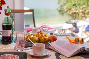 Una mesa con una botella, un frutero, una taza, un vaso y un libro.